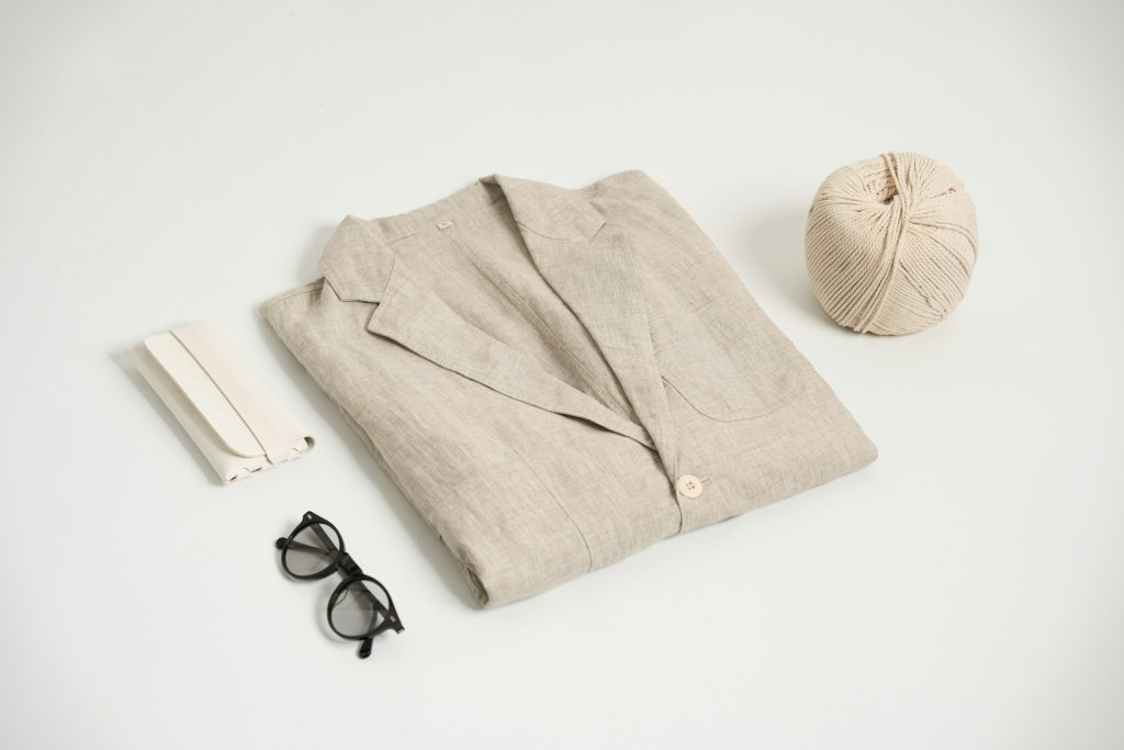 A folded linen shirt with glasses and a hat on a light background