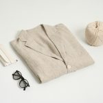 A folded linen shirt with glasses and a hat on a light background