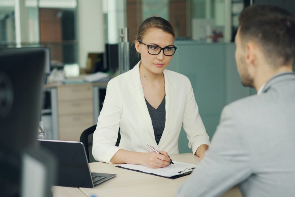 A woman in a white blazer at a job interview across a desk