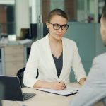 A woman in a white blazer at a job interview across a desk