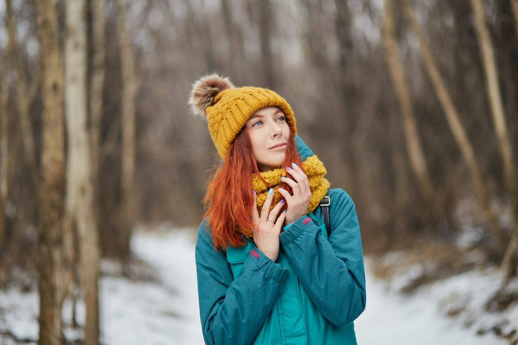 A woman in a teal winter jacket and yellow toque in a snowy forest