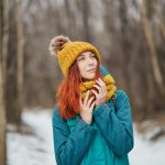 A woman in a teal winter jacket and yellow toque in a snowy forest
