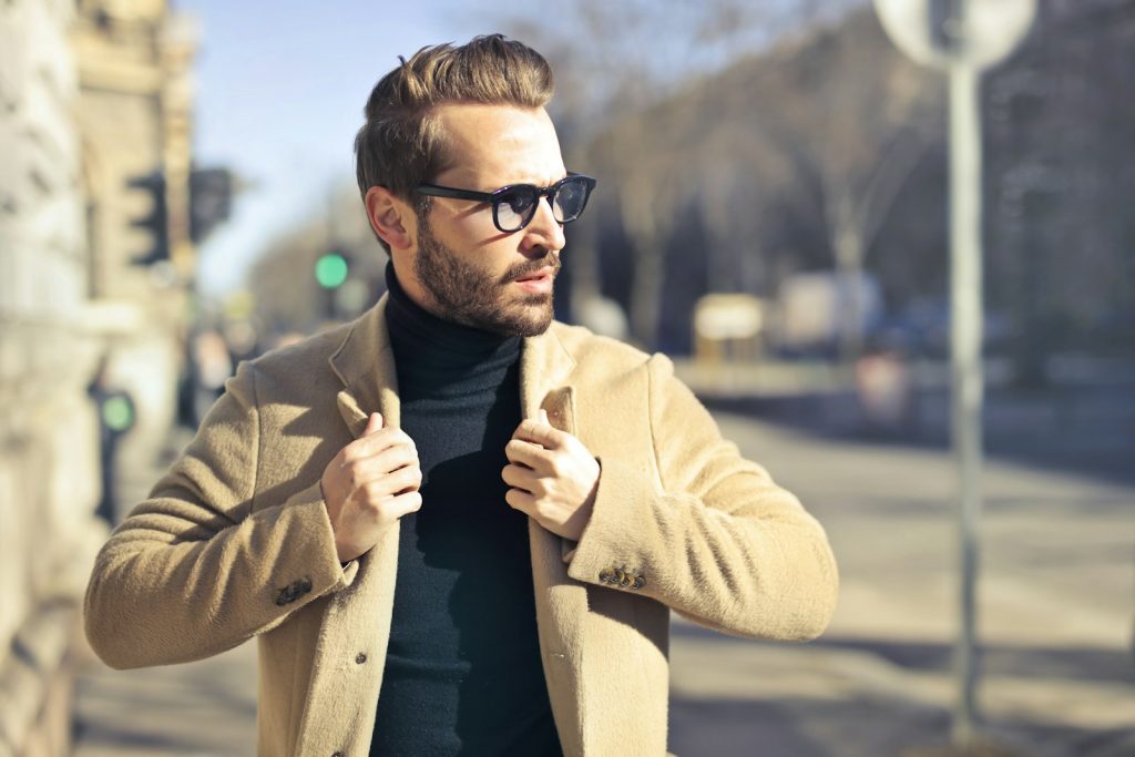 A man in a camel coat and black turtleneck on a city street