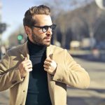 A man in a camel coat and black turtleneck on a city street